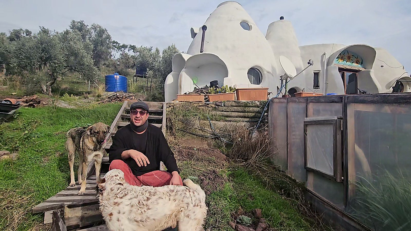 Host sitting with the farm dogs in front of the superadobe domes